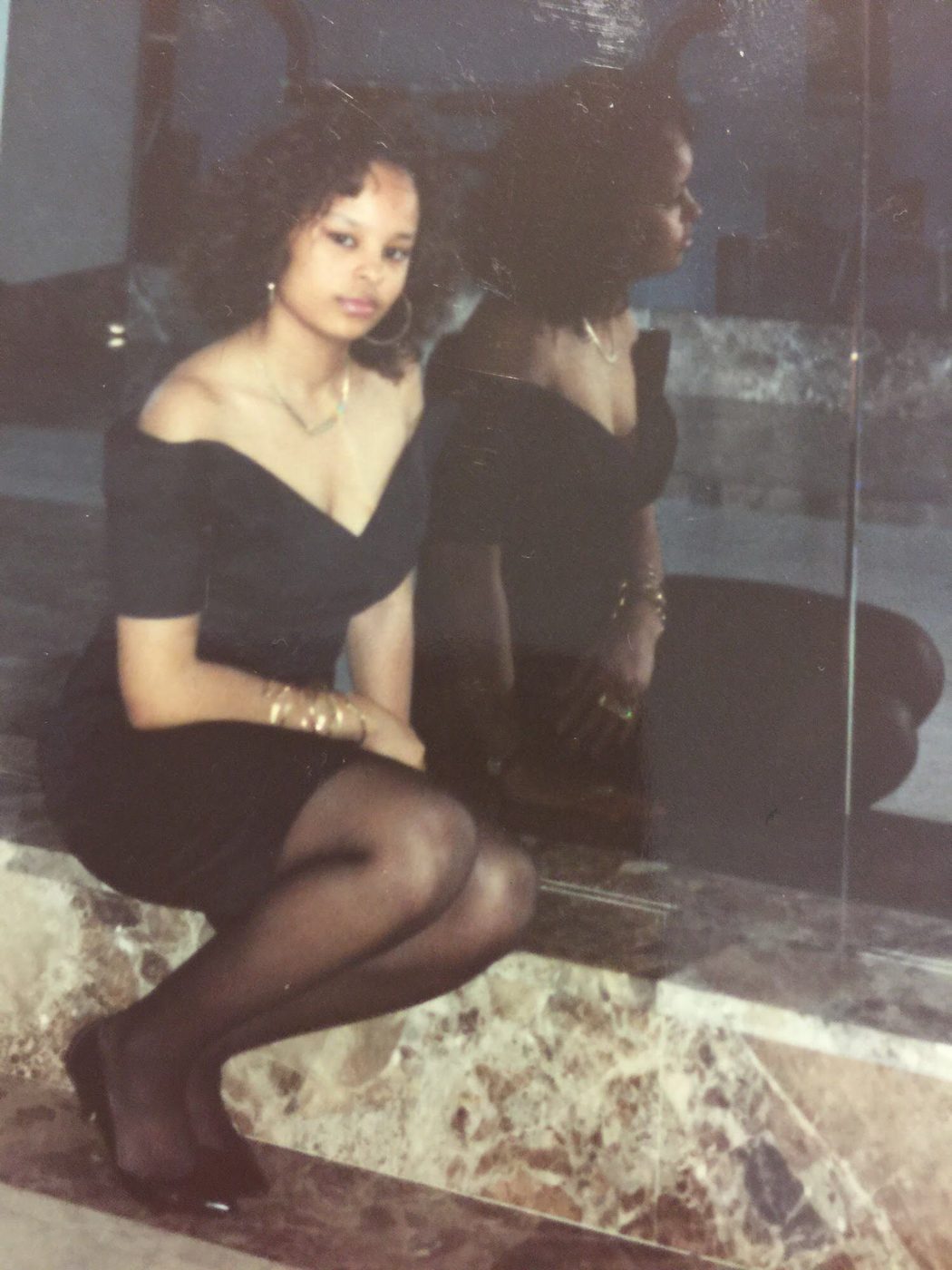 Sonya in a black off-the-shoulder dress, seated by a mirror