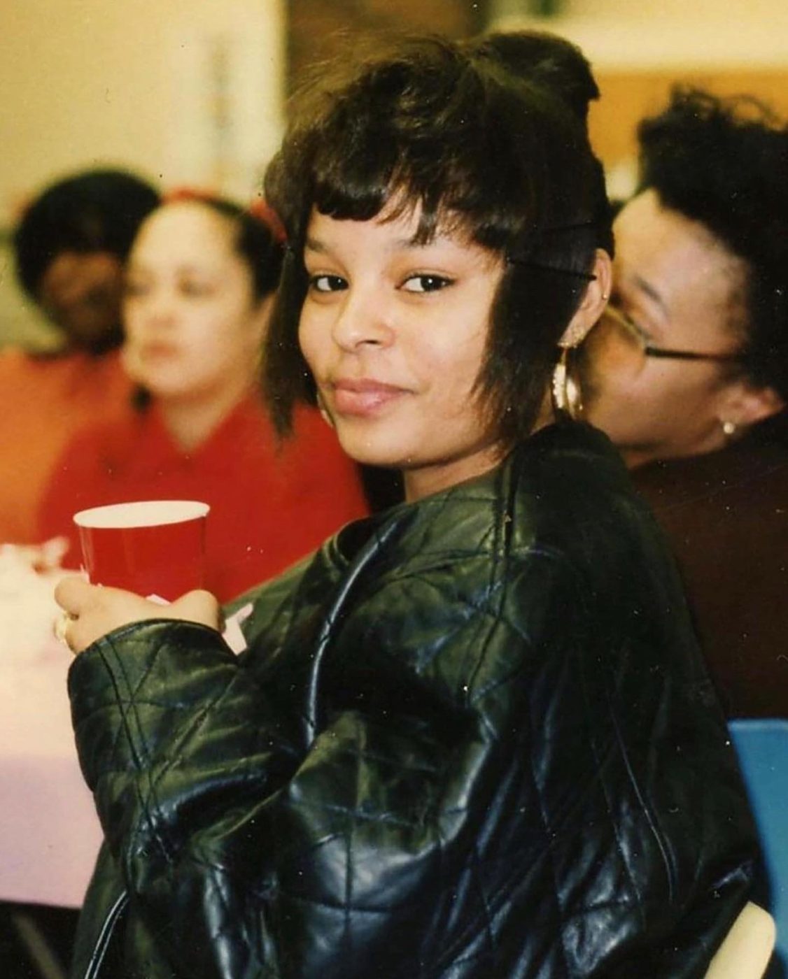 Sonya in a black leather jacket, smiling over her shoulder at a gathering