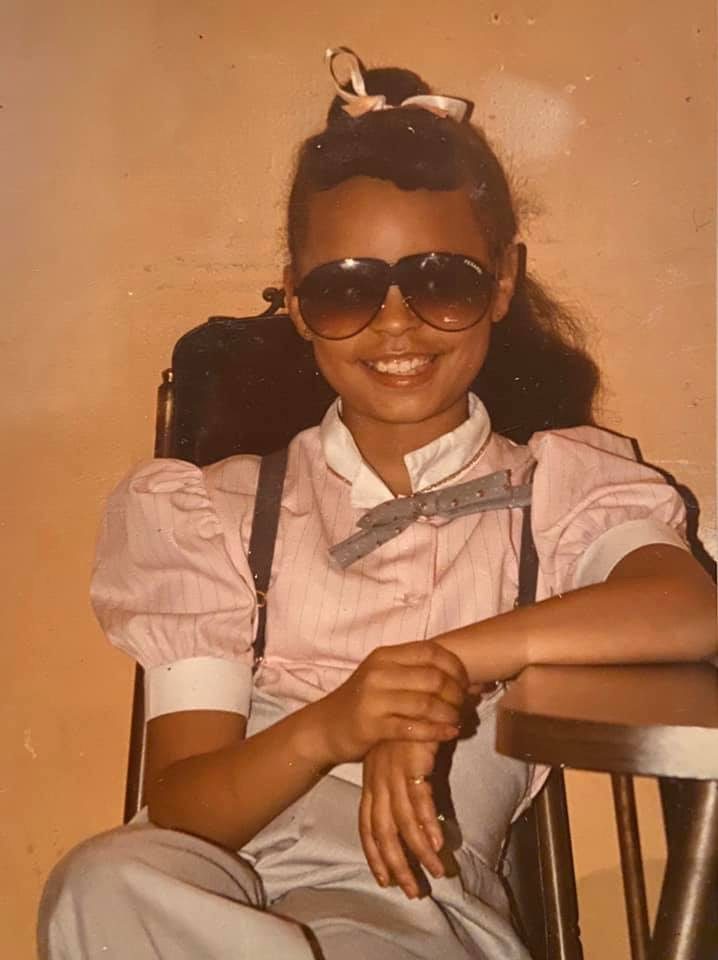 Sonya as a girl wearing big sunglasses and smiling